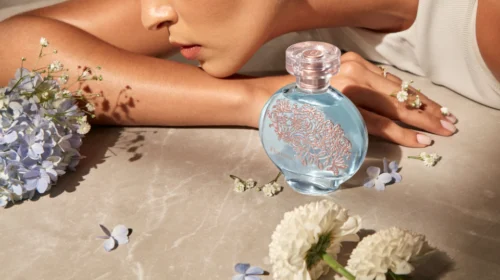 Perfume azul com detalhes florais e mãos.