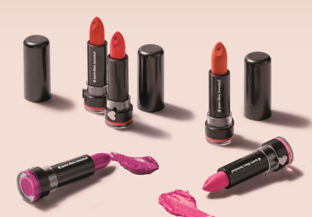 Several open lipsticks in red, pink, and purple shades on a light pink surface.