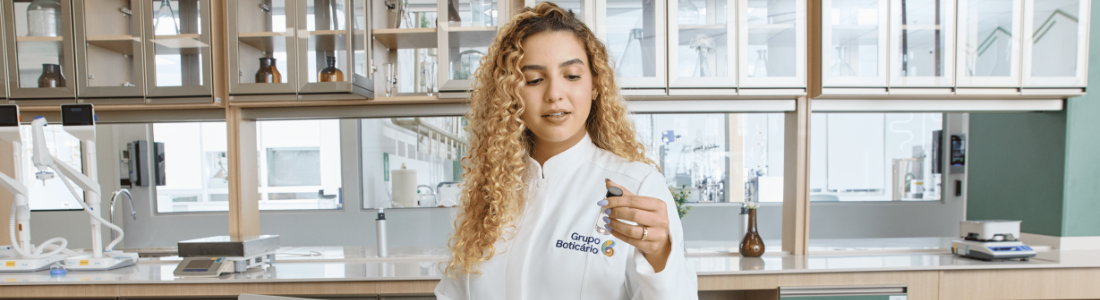 Scientist in a white lab coat holding a small vial in a modern laboratory.