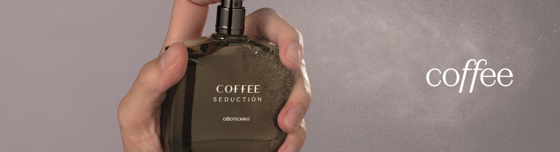 Mão borrifando o perfume Coffee Seduction, com a névoa visível sobre um fundo cinza suave.