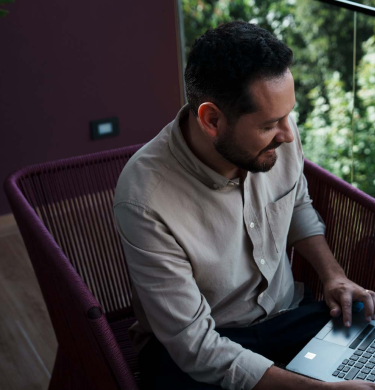 Na foto, há a imagem aproximada das mãos de um homem com pele negra, camisa social azul e calça social preta utilizando um notebook.
