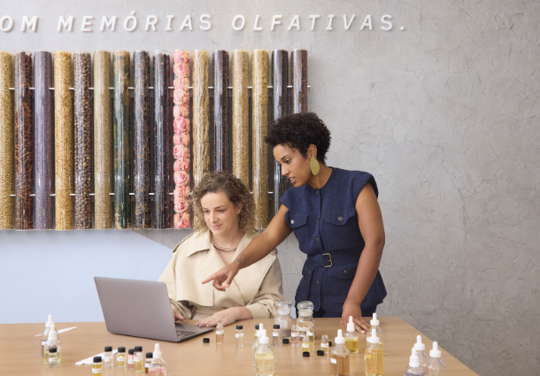 Duas mulheres em um laboratório olfativo, trabalhando juntas em um laptop.