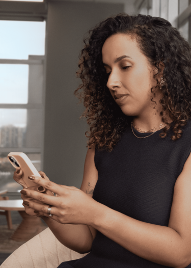 Mulher sentada usando o celular em ambiente corporativo, com expressão concentrada.