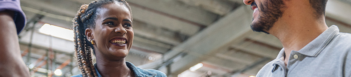 Imagem de pessoas sorrindo e se olhando. Em destaque está uma mulher negra de tranças sorrindo, ela veste uma jaqueta jeans