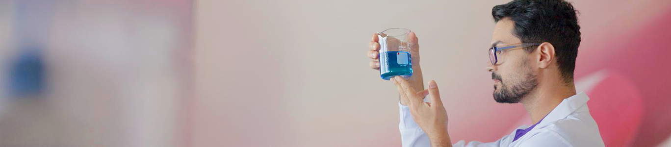 Imagem de homem pesquisador com frasco químico na mão, olhando o conteúdo azul dentro do frasco