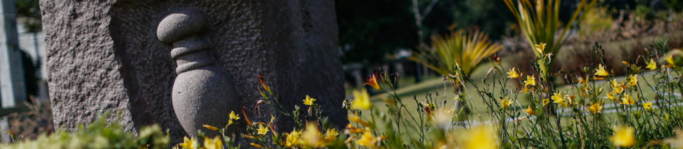 Imagem de escultura de cimento da ânfora de O boticário no meio de flores de jardim