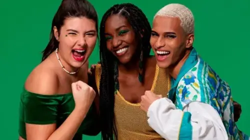 Campanha Quem Disse, Berenice? e Guaraná Antarctica se juntam para torcer pelo Brasil com coleção inspirada nas cores do país - na frente do fundo verde temos três torcedores brasileiros, da esquerda para direita tem uma mulher branca com rabo de cavalo preso, acessório branco no pescoço, veste um cropped verde da cor da bandeira e está com punho cerrado e expressão de grito e energia. Ao lado dela tem uma mulher negra com tranças pretas longas, ela está sorrindo e veste uma regata cor de amarelo com furinhos. Ao lado têm um homem negro. Ele tem cabelos bem curtos e cor branca. Veste uma blusa com magas longas acor azul claro e branco. Também está com o punho cerrado e expressão de grito e energia