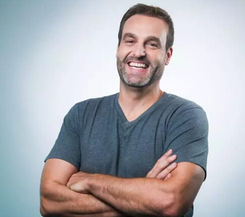 imagem do Eduardo Javarotto. Homem, branco, com cabelos castanhos, barba grizalha. Ele está sorrindo para foto e veste camiseta cinza, com braços cruzados
