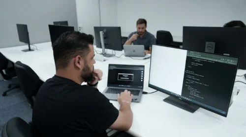 Imagem de um colaborador do Grupo Boticário em frente a um monitor e a um notebook. Foto ilustra uso de inteligência artificial no mercado da beleza.