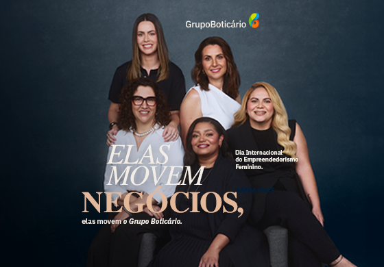 Na imagem do banner, em um fundo preto, iluminado no centro, temos cinco mulheres lado a lado, sorrindo e posando para a câmera. Da esquerda para a direita, a primeira mulher está em pé. Ela é branca de olhos castanho-escuros e cabelos lisos e castanhos, veste uma camiseta preta e usa um relógio preto no punho esquerdo. Na frente dela, temos a segunda mulher, que está sentada. Ela é uma mulher madura, branca, de olhos castanho-escuros e cabelos encaracolados pretos, na altura dos ombros. Ela veste uma camisa branca e uma calça preta, usa um colar de pérolas brancas, um relógio no punho esquerdo e óculos de grau de armação marrom. Em pé, ao lado da primeira mulher, temos a terceira. Ela é branca de olhos e cabelos castanho-escuros. Ela veste uma regata branca de um ombro só. Na frente dela, sentada, temos a quarta mulher. Ela é negra de olhos castanho-escuros e cabelos lisos e pretos. Ela veste uma blusa preta sobreposta por um cardigan preto e usa um colar dourado. Ao lado dela, temos a última. Ela é uma mulher branca de olhos castanho-escuros e cabelos loiros ondulados. Ela veste uma blusa preta sobreposta por um colete preto. Centralizado, em letras beges e na cor salmão, o texto: “Dia Internacional do Empreendedorismo Feminino. Elas movem negócios, elas movem o Grupo Boticário.”. Logo do Grupo Boticário centralizada no topo.