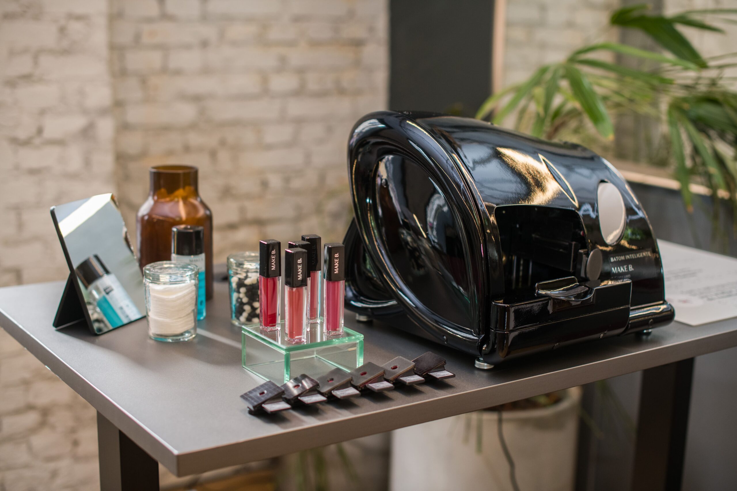 A display of multiple lipsticks arranged on a table alongside a stylish handbag and various bottles, showcasing products from Grupo Boticário.
