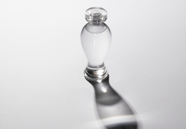 Imagem de um frasco de perfume com reflexo sobre fundo cinza.