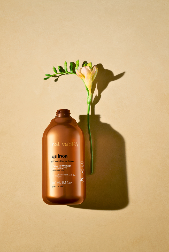 Frasco da linha Nativa SPA de O Boticário disposto sob fundo alaranjado com uma flor ao lado.