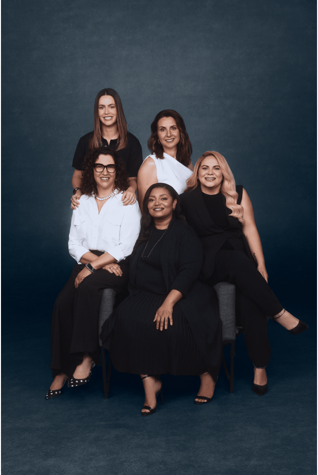 Imagem de cinco mulheres sentadas posando para foto.