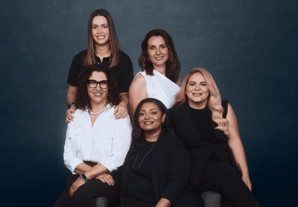 Imagem de cinco mulheres sentadas posando para foto.