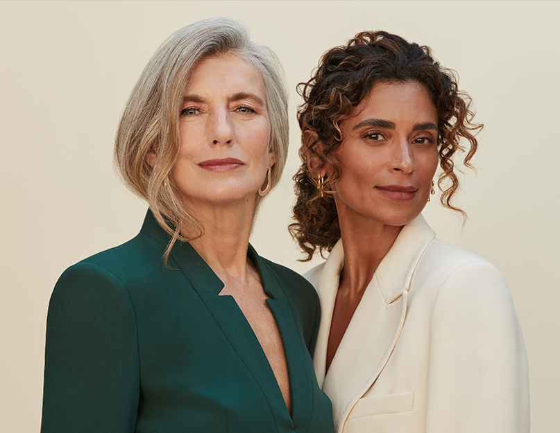 Duas mulheres elegantes posam lado a lado, usando ternos verde escuro e branco.