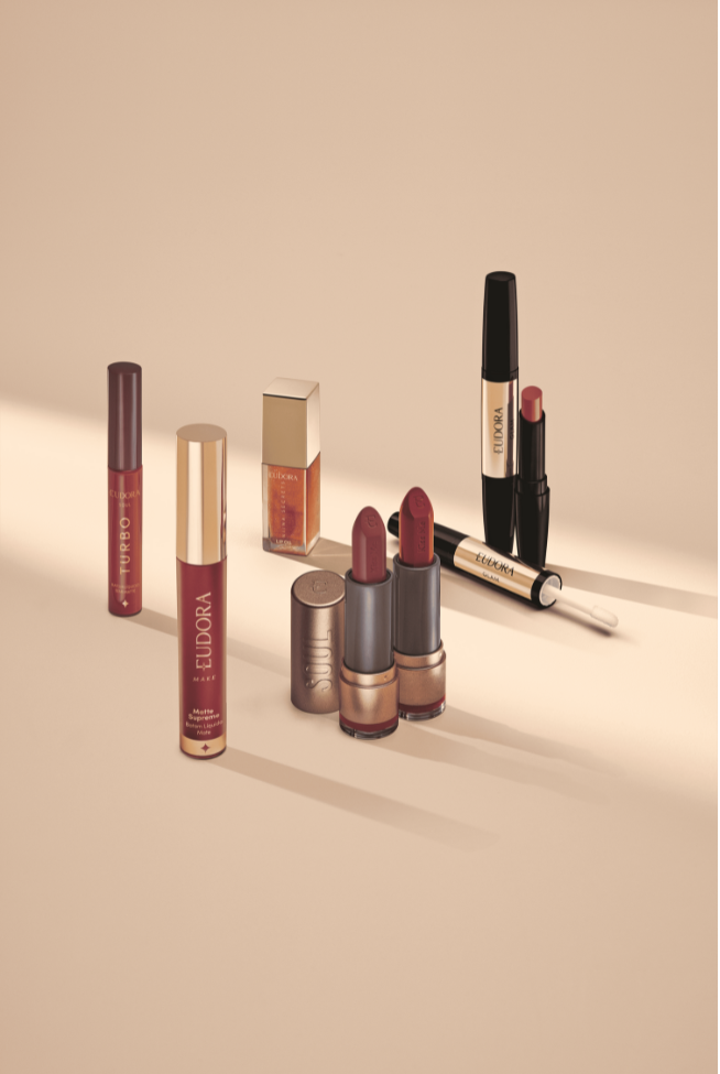 Exposição de produtos de maquiagem Eudora, incluindo batons e gloss, em tons de vermelho e nude.