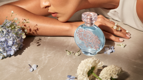 Perfume azul com detalhes florais e mãos.