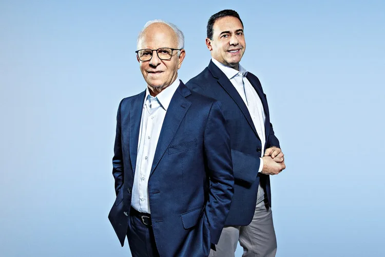 Dois homens de terno posam em fundo azul.