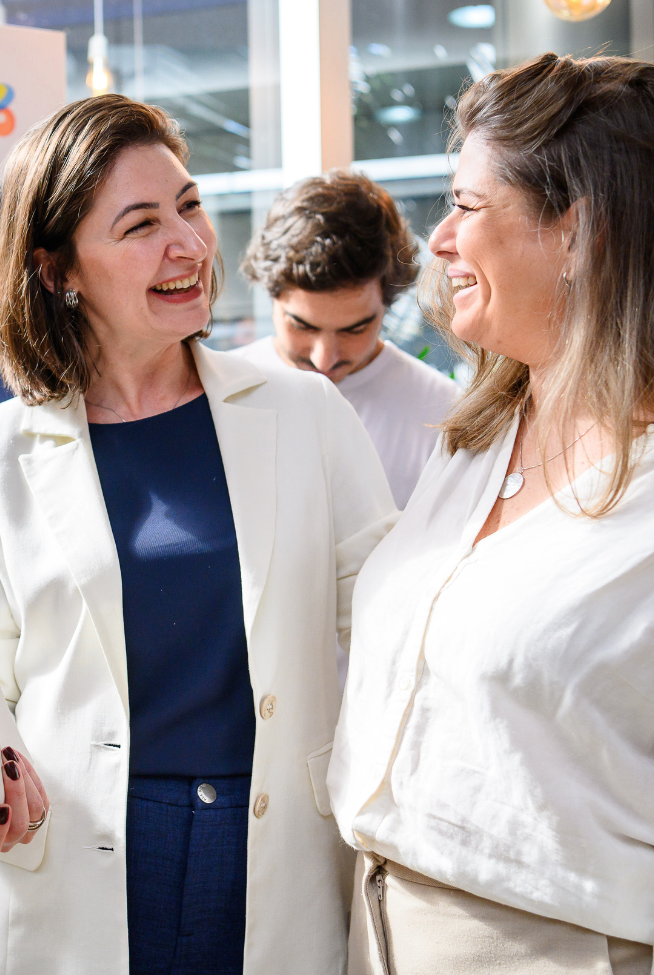 Duas mulheres sorrindo e conversando, com fundo de "Grupo Boticário Startups".