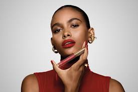 Mulher com batom vermelho vibrante segura o produto próximo ao rosto com expressão confiante.