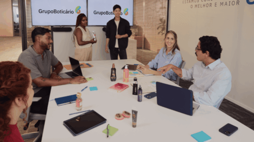 Reunião entre pessoas diversas em sala do Grupo Boticário, com laptops, anotações e produtos sobre a mesa.
