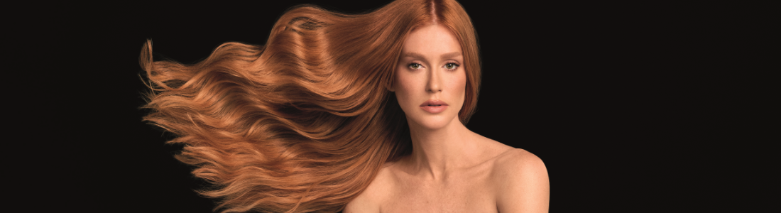 Mulher ruiva, cabelo longo e ondulado em movimento, ombros nus, em fundo preto.