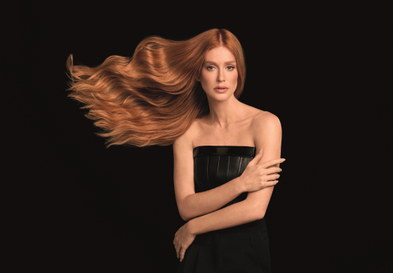 Mulher ruiva, cabelo longo e ondulado em movimento, ombros nus, em fundo preto.