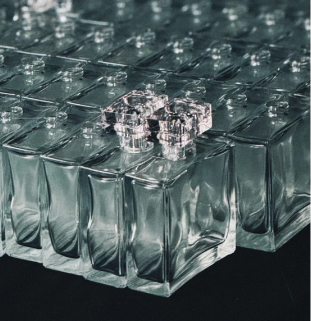 A fotografia mostra um conjunto de frascos de perfume enfileirados sobre um plano de fundo neutro na cor cinza.