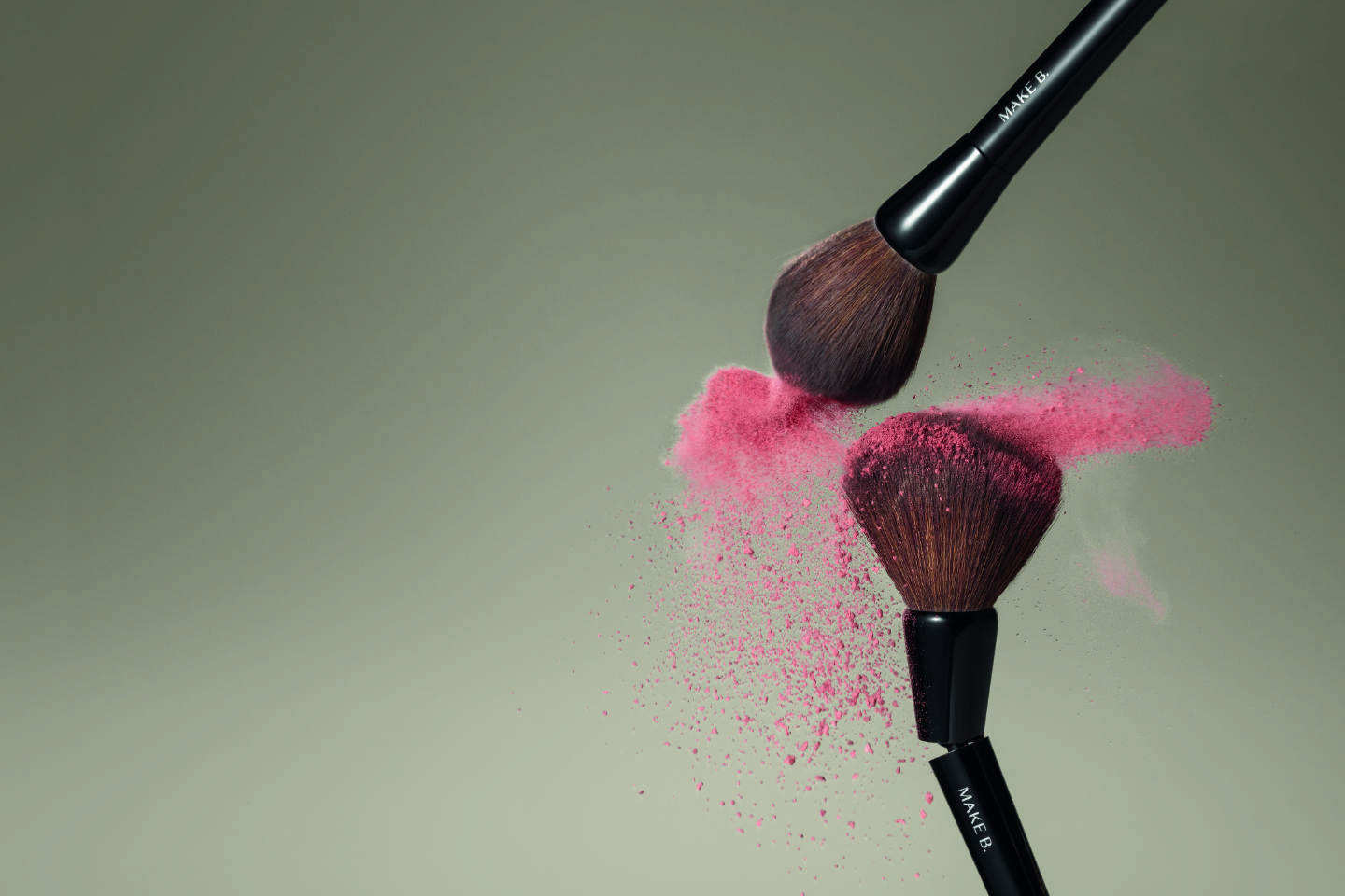 A imagem mostra dois pincéis da linha MakeB depositando uma névoa de blush rosa sobre um plano de fundo neutro na cor marrom.
