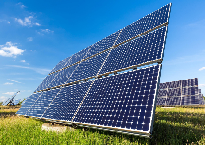 A fotografia mostra uma imagem aproximada de diversas placas solares em um ambiente a céu aberto.